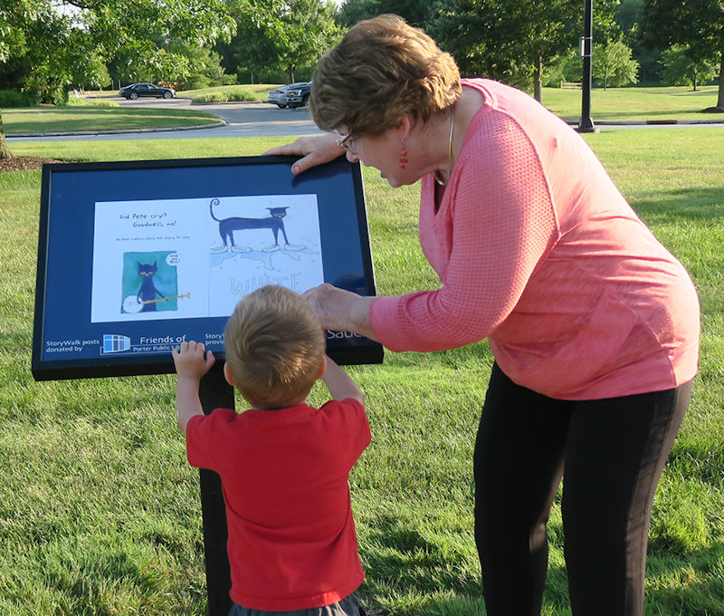 Lynn Pettyjohn of the Friends shows a young patron a page from the StoryWalk